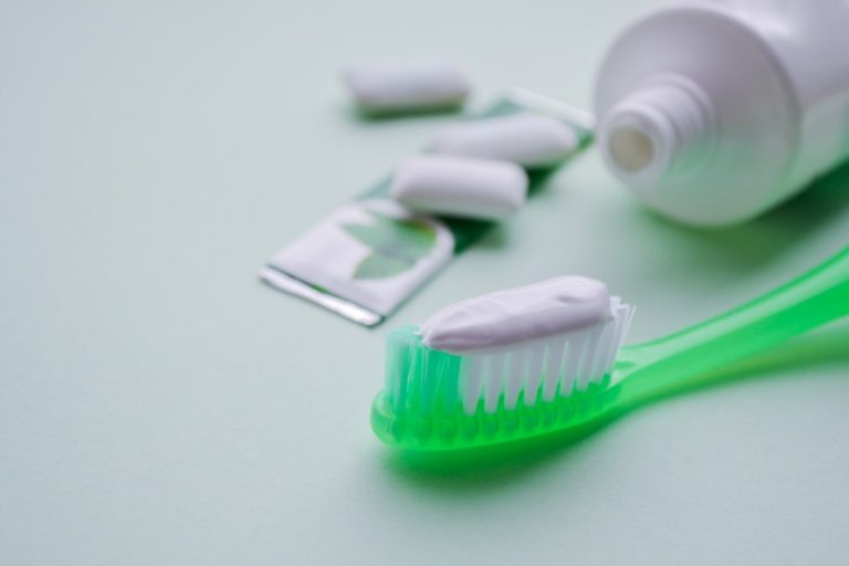 a-green-toothbrush-with-toothpaste-tube-of-toothpaste-a-plate-of-mint-gum-and-white-gum-pads-on-a_t20_2wpda8-768x512