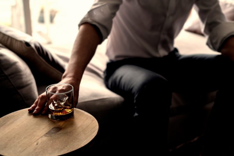 man-reaching-for-whiskey-on-ice-alcoholic-cocktail-liquor-drink-while-sitting-on-a-comfy-lounge-chair_t20_QKmBkE-768x513